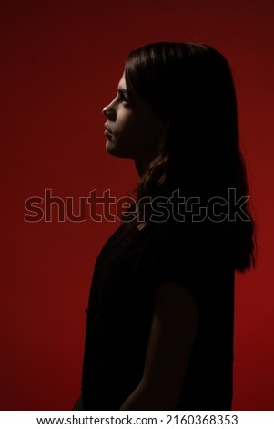 Red silhouette rim lighting against dark studio background. Face contour on red background. Beauty and fashion concept. Black silhouette of a beautiful young woman on red background. Light on a face