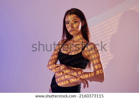 Orange colored woman word. Beautiful young woman is in projector neon lights in the studio.