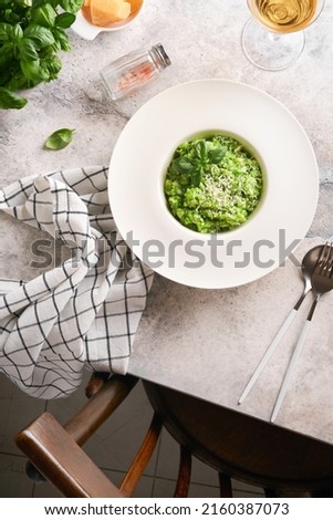 Italian risotto. Delicious risotto in white plate with pesto sauce or wild garlic pesto, basil, parmesan cheese and glass of white wine on old light grey table background. Top view with copy space.