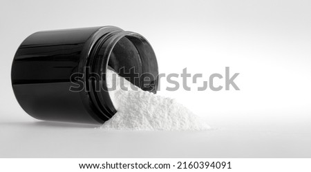 Sports nutrition -  protein. Measuring spoon and white medicinal powder with black jar on white background, isolated. Nutritional supplement or medicament, medicine treatment concept Royalty-Free Stock Photo #2160394091