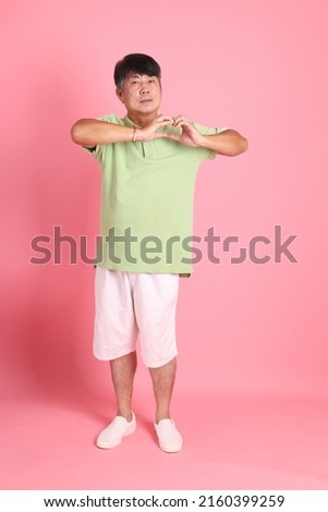 The senior Asian man with casual clothes standing on the pink background.
