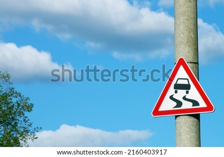 Road sign "Slippery road" on a concrete pole against the blue sky
