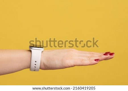 Closeup side view of woman hand with red manicure and wristtwatch with white strap, technology device. Indoor studio shot isolated on yellow background.
