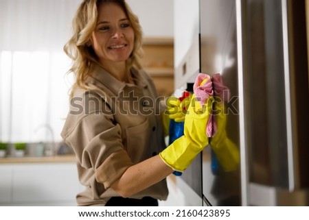 Woman wiping stainless steel refrigerator door with rag and cleaning agent. Housewife cleans the kitchen Royalty-Free Stock Photo #2160423895