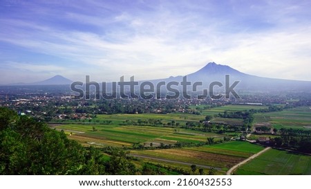 The view of Mount Merapi and the expanse of rice fields in Yogyakarta as seen from the direction of the "Riyadi" spot, which is the name of one of the tourist destinations                        Royalty-Free Stock Photo #2160432553
