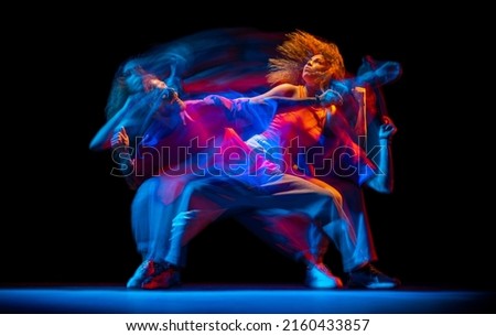 Freestyle. Young man and woman dancing hip-hop in sportive style clothes on dark background at dance hall in mixed neon light. Youth culture, hip-hop, movement, style and fashion, action.