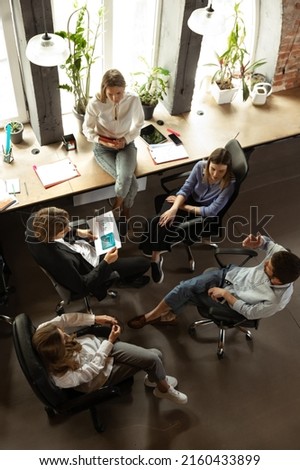 Young people talking, working with colleagues, co-workers at loft style office. Business, urban lifestyle, work, finance, tech concept. Serious and smiling men and women, manager and subordinates. Royalty-Free Stock Photo #2160433899