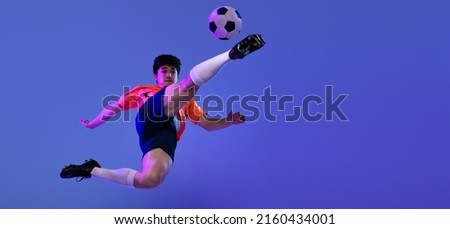Kick the ball. Studio shot of male professional football, soccer player practicing with ball isolated on purple background. Concept of sport, match, ad, active lifestyle. Flyer with copy space for