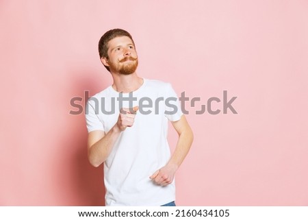 Dreaming, having doubts. Half-length portrait of young happy man in white t-shirt posing isolated on pink background. Concept of art, fashion, emotions, aspiration. Copy space for ad