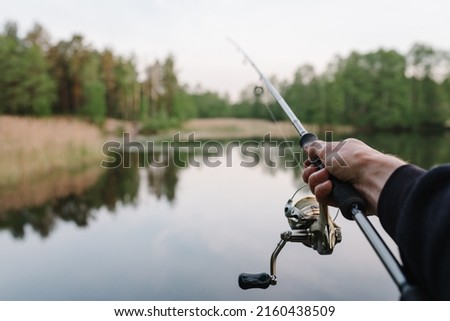 Fisherman with rod, spinning reel on the river bank. Man catching fish, pulling rod while fishing from lake or pond with text space. Fishing for pike, perch on beach lake or pond. Fishing day concept. Royalty-Free Stock Photo #2160438509