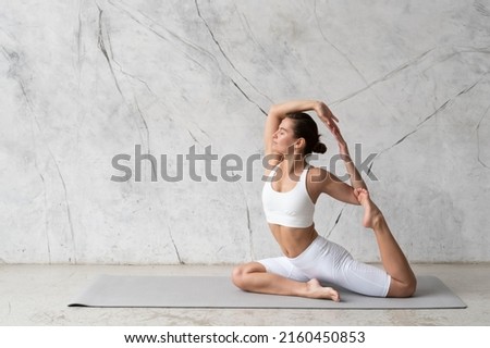 Young woman practicing yoga One-Legged King Pigeon Pose, Eka Pada Rajakapotasana against texturized wall