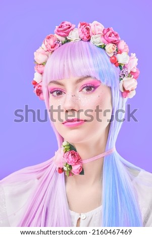 Beauty, makeup and hairstyle. Portrait of a pretty teen girl with bright pink make-up posing in colored violet-blue wig and flower wreath on the head. Soft purple background. 