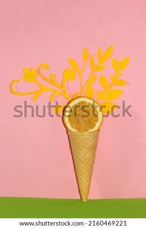 ice cream cone with slice lemon, yellow paper leaves and flowers come out of lemon, creative art summer design, pink-green background, trendy colors