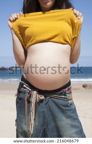 pregnant woman showing her navel at Asturian beach