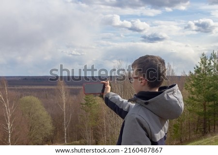 A teenage boy takes pictures on a smartphone of the landscape of a swamp in spring or autumn.