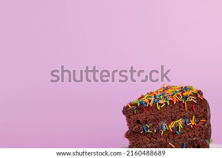 Slice of birthday cake decorated colorful sprinkles on pink background. Chocolate cake slice, Birthday party minimal concept, close up image.