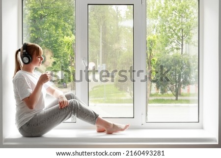 the woman on the window listens to music and drinks tea. meditation at home