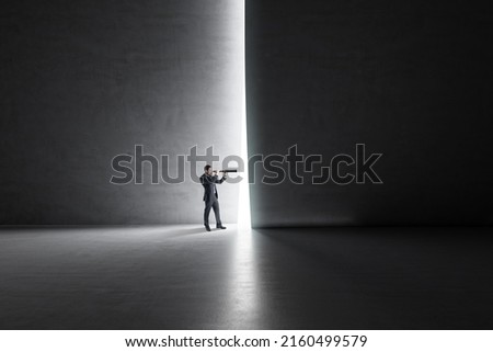 Looking in the future and busines development concept with businessman back view using spyglass looking through a light hole in a dark wall in empty spacious hall Royalty-Free Stock Photo #2160499579