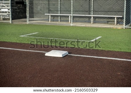 Angled view of a white base on a baseball field, with the view of a dugout in the background