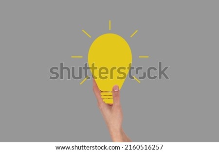 Hand holding glowing light bulb. Idea, inspiration, creativity concept on grey background. High quality photo