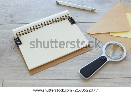 open notebook with a spiral near an envelope and a magnifying glass