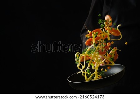 A bright assorted mix of seafood, vegetables, herbs and Italian pasta in a frying pan. Seafood recipes. Restaurant and home cooking. Food in a frozen flight on a black background.
