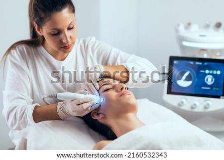 Shot of cosmetologist making ultrasonic cleaning and rejuvenation the face to beautiful woman on the spa center. Royalty-Free Stock Photo #2160532343