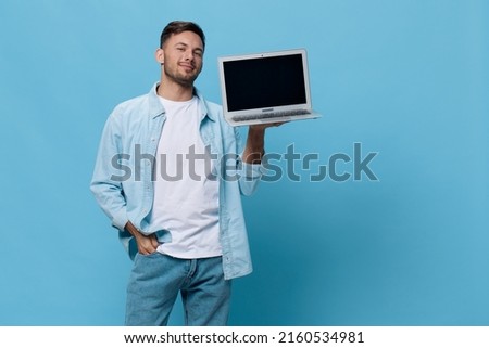 Attractive smiling tanned handsome man in casual basic t-shirt show laptop screen recommended gadget posing isolated on blue studio background. Copy space Banner Mockup. Electronics repair IT concept