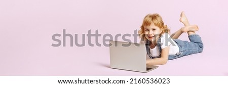 Banner smiling child in denim jumpsuit lies with an open laptop on a white background.