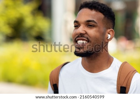 Closeup Portrait Of Happy Black Man Listening To Music Wearing Wireless Headphones Walking Outdoors In The City, Free Copy Space. Male Relaxing Outside On Sunny Day Enjoying Favorite Song