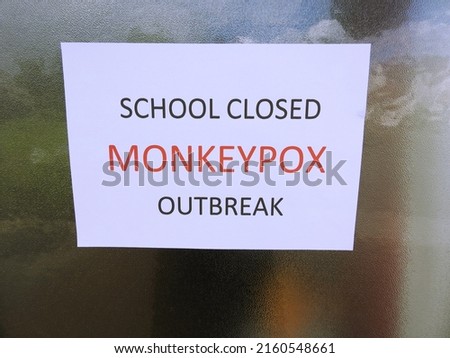 'School Closed Monkeypox Outbreak' wording on A4 paper stuck to reflective speckled glass window. 
