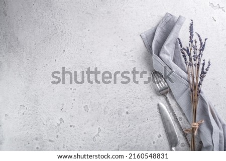 Grey concrete background with a light textile napkin, a bunch of lavender and tableware. Food background for a recipe or design. Top view, space for text