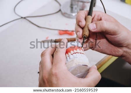 Close up of a technician who carves the wax, acrylic and plaster in the process of making dentures Royalty-Free Stock Photo #2160559539