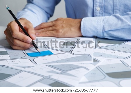 Man holding a pencil pointing to cadastral map to decide to buy land. real estate concept with vacant land for building construction and housing subdivision for sale, rent, buy, investment