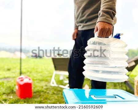 Folding water tank held by a man at a campsite