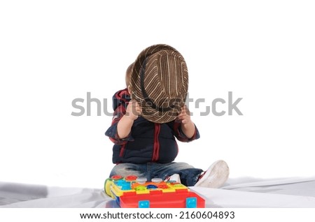 Child covers his face with brown woven cap on white background