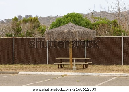 An isolated smoking area with a picnic table, a palapa umbrella and an ashtray receptacle.
