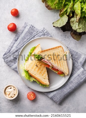 Club sandwich on a blue plate and napkin of ham cheese, cucumber, tomato and lettuce leaves close-up on a blue background with mayonnaise. Top view. Royalty-Free Stock Photo #2160615521
