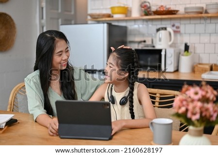 Kind and cheerful Asian mom encourage her daughter for studying an online class at home. Homeschooling during quarantine.