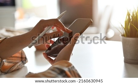 Female hands holding a smartphone and stylus pen, using smartphone, searching some information on the internet. cropped image