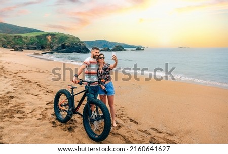 Young couple with fat bike taking a selfie with the mobile on the beach