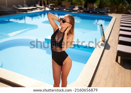 Fit woman in bikini sunbathing and chilling near swimming pool at a tropical spa. Attractive slim girl in swimwear and sunglasses posing at luxury resort. Hot female relaxing and enjoying the sun.
