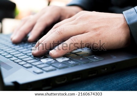 Remote work concept. Male hands typing on the notebook keyboard. Young caucasian man using laptop at home while sitting the wooden table. Man using laptop for online working at home. Royalty-Free Stock Photo #2160674303