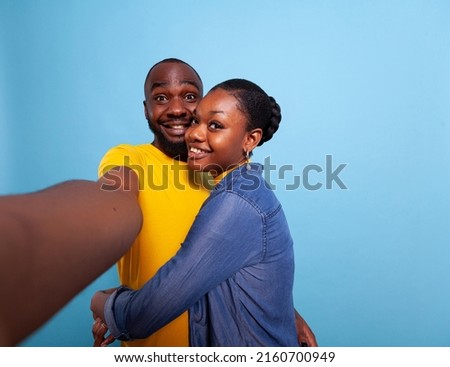 POV ofcheerful lovers in relationship in front of camera, taking pictures together in studio. Cheerful couple using phone in hand to take selfies and share romance. Partners hugging each other
