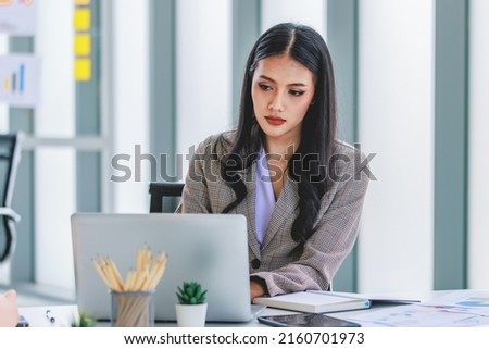 Asian young pretty thoughtful concentrated female professional successful businesswoman in formal business suit sitting holding pen at chin thinking about customer job task solution ideas with laptop.