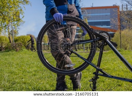Man reparing bicycle wheel. Cyclist changing tire diy. Looking for bicycle tires leak. Examining bike for issues in park. Back bicycle tire wobbles problem solving. Royalty-Free Stock Photo #2160705131