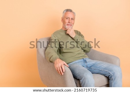 Photo of calm elder grey hairdo man sit look promo wear green pullover jeans isolated on beige color background