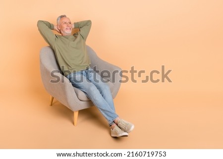 Full length photo of think elder grey hairdo man sit look up wear pullover jeans sneakers isolated on beige background