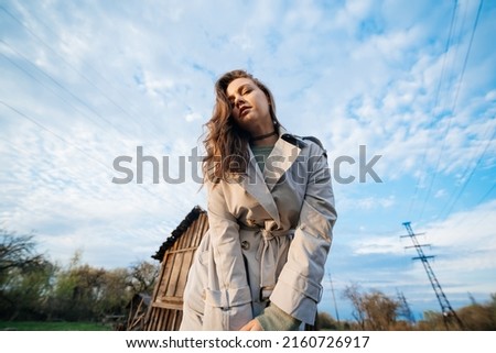 beautiful girl with long hair in a grey trench coat  blue sky background outdoors in spring