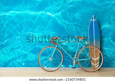 Bicycle and surfboard near wall with print of clear water